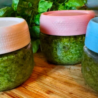 Close-up of three pastel ceramic pots (peach, pink, blue) with textured sides on a wooden surface, greenery in the background, a decorative scene.