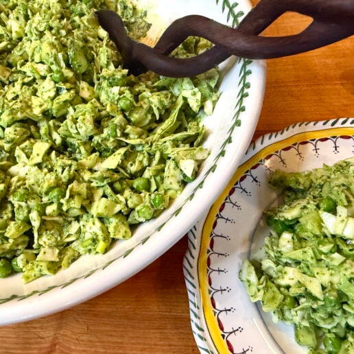 Large white bowl of chopped avocado salad with herbs, a wooden spoon resting on top, on a wooden table.