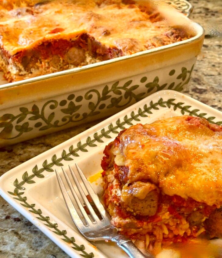 Cheesy baked meat and rice casserole served on a white plate with a fork nearby.