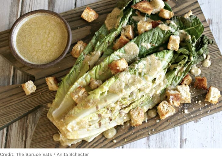 Wedge of romaine lettuce drizzled with Caesar dressing and scattered croutons on a wooden board.